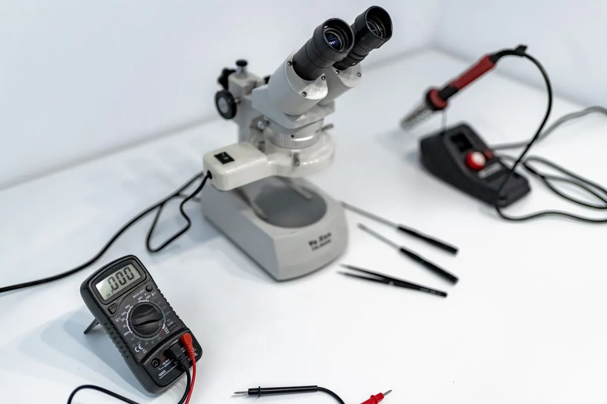 Technician tracing circuit paths on a board under a workbench microscope